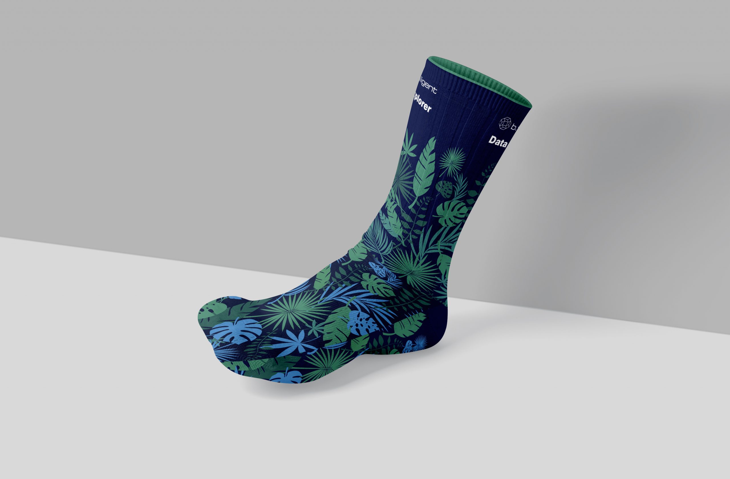 Data Explorer-Socken für b.telligent auf der FabCon Europe: Dunkelblaue Socken mit grün-blauen Dschungel-Pflanzenmotiven und den Aufdrucken ‚b.telligent‘ und ‚Data Explorer‘. Entworfen von Rebekka Markert, Grafikdesigner:in für kreative Merchandise-Ideen.