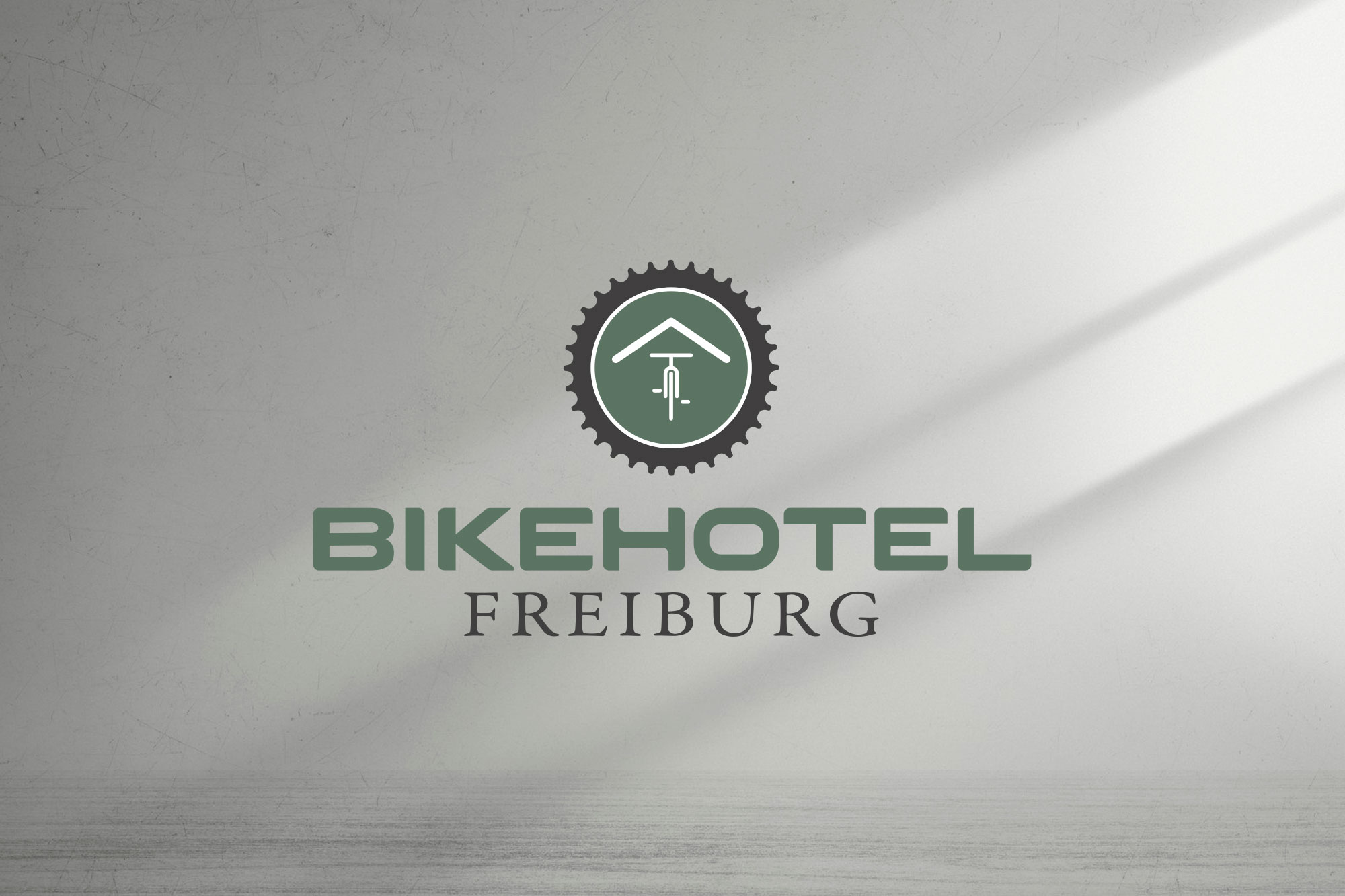 Bikehotel Freiburg Logo in Form eines grünen Zahnkranzes mit weißem Hausdach und Fahrrad-Silhouette.